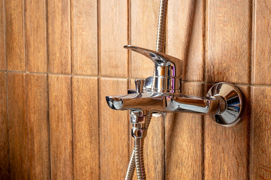 Showerhead and faucet are mounted on wood-look tiles.